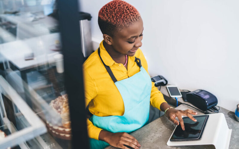 Female worker of pastry shop working with tablet at counter